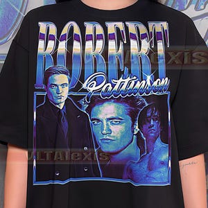 Op de afbeelding: Zwart T-shirt met een grafische print van Robert Pattinson. Het ontwerp bevat de naam "ROBERT PATTINSON" in een retro lettertype en drie afbeeldingen van de acteur in blauw- en paarstinten.