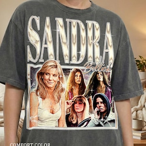 May include: Dark gray t-shirt featuring a vintage-style graphic of Sandra Bullock with the text "SANDRA Bullock" in a decorative font. The shirt also has the words "COMFORT COLOR" and "PEPPER" printed on it.