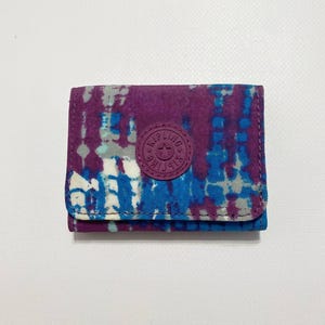 Peut inclure: Un petit portefeuille à motif tie-dye violet et bleu avec un logo rond rouge orné d'une étoile blanche.
