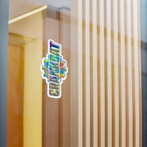 May include: A holographic sticker with the word "GRINDAT" in a vertical layout. The text is in a bold, sans-serif font, with a rainbow gradient effect. The sticker has a gear-shaped design around the text.