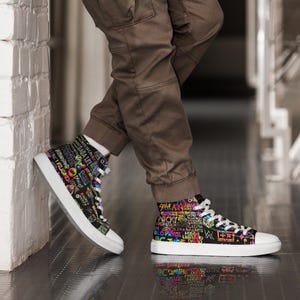 Könnte beinhalten: Schwarze High-Top-Sneaker mit weißer Sohle und Schnürsenkeln. Die Sneaker sind mit farbenfrohem Text und Grafiken bedeckt. Getragen von einer Person, die eine braune Hose und weiße Socken trägt.