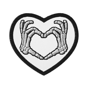 Könnte beinhalten: Schwarz-weiß gestickter Patch mit zwei Skeletthänden, die eine Herzform bilden. Der Patch hat die Form eines Herzens und einen schwarzen Umriss.