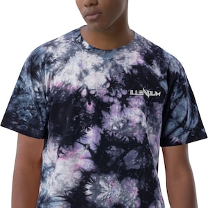 May include: A tie-dye t-shirt in shades of black, white, and purple. The shirt features the word "ILLENIUM" in white, stylized text on the upper chest. The short-sleeved shirt has a crew neck.