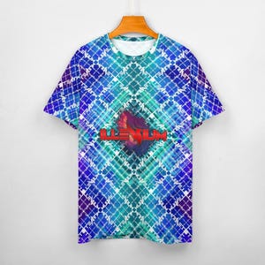 May include: A short-sleeved t-shirt with a vibrant, geometric pattern in shades of blue, teal, and purple. The shirt features the word "ILLENIUM" in red block letters over a stylized graphic. The shirt is hanging on a wooden hanger.