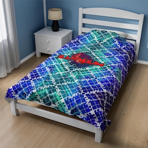 Puede incluir: Una cama individual con una manta estampada en azul, verde y morado. La manta presenta un diseño de texto blanco repetido y un gráfico rojo central. El marco de la cama es blanco y la habitación tiene paredes azules.