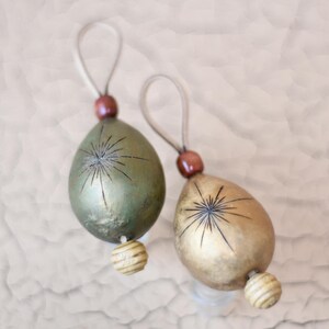 Op de afbeelding: Twee handgemaakte kerstversieringen met een stervormig ontwerp. Een versiering is groen met gouden accenten en de andere is goud met bruine accenten.