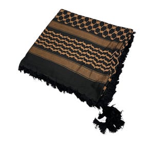 Puede incluir: Bufanda keffiyeh negra y marrón doblada, con un patrón geométrico detallado y bordes con flecos. El diseño de la bufanda se muestra de forma destacada, mostrando su textura y combinación de colores.