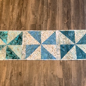 May include: A blue and white table runner with a pinwheel pattern. The runner is made of fabric with a variety of patterns, including paisley and geometric designs.