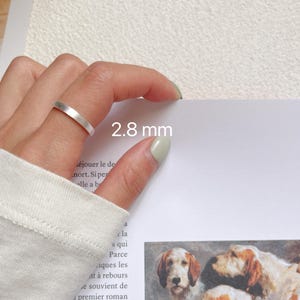 May include: A silver ring with a 2.8 mm width. The ring is shown on a finger.