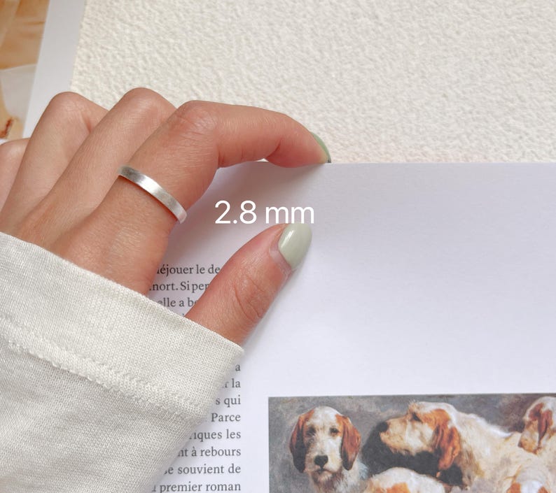 May include: A silver ring with a 2.8 mm width. The ring is shown on a finger.