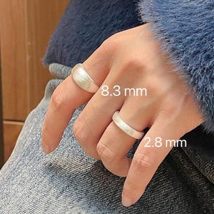 May include: Two silver rings on a finger. The larger ring is 8.3 mm wide and the smaller ring is 2.8 mm wide.