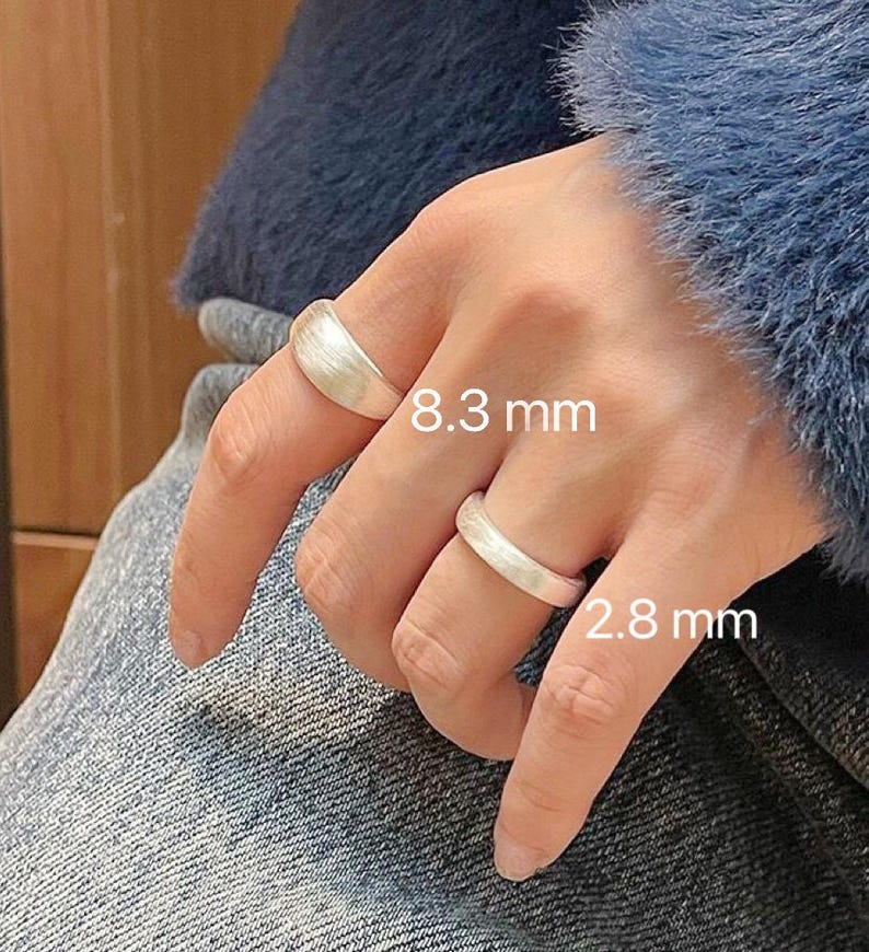 May include: Two silver rings on a finger. The larger ring is 8.3 mm wide and the smaller ring is 2.8 mm wide.