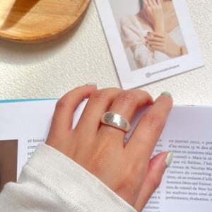 May include: A silver ring with a textured, hammered finish. The ring is wide and has a rounded shape.