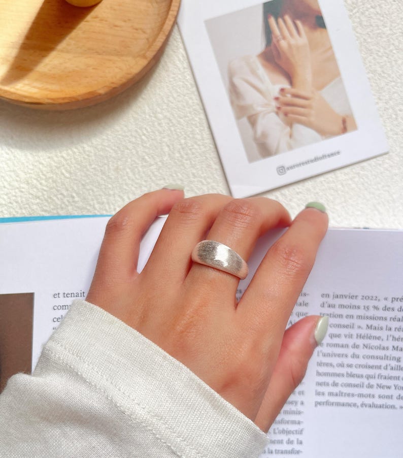 May include: A silver ring with a textured, hammered finish. The ring is wide and has a rounded shape.