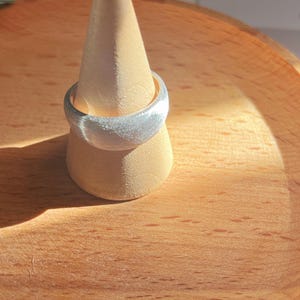 May include: A silver ring with a textured finish, displayed on a wooden ring holder.
