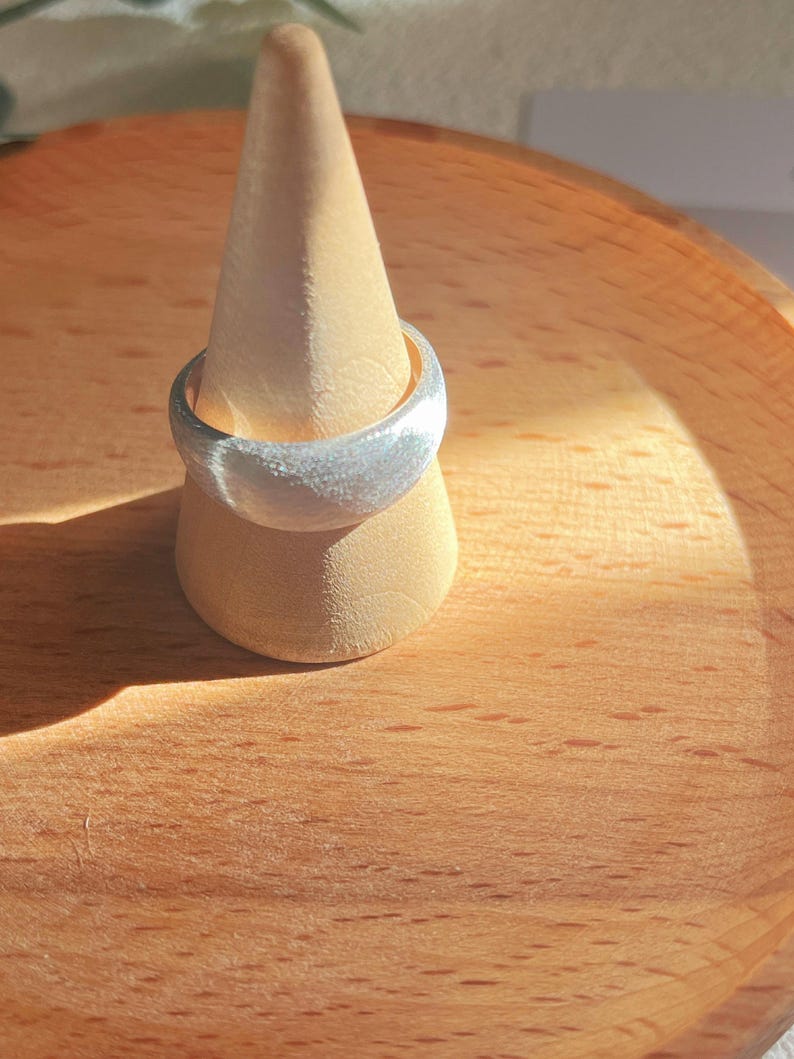 May include: A silver ring with a textured finish, displayed on a wooden ring holder.