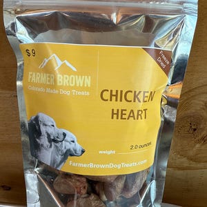 May include: A silver metallic bag of Farmer Brown Chicken Heart dog treats. The bag has a yellow label with the text "CHICKEN HEART" and a weight of 57 grams. The bag also features a picture of two dogs.