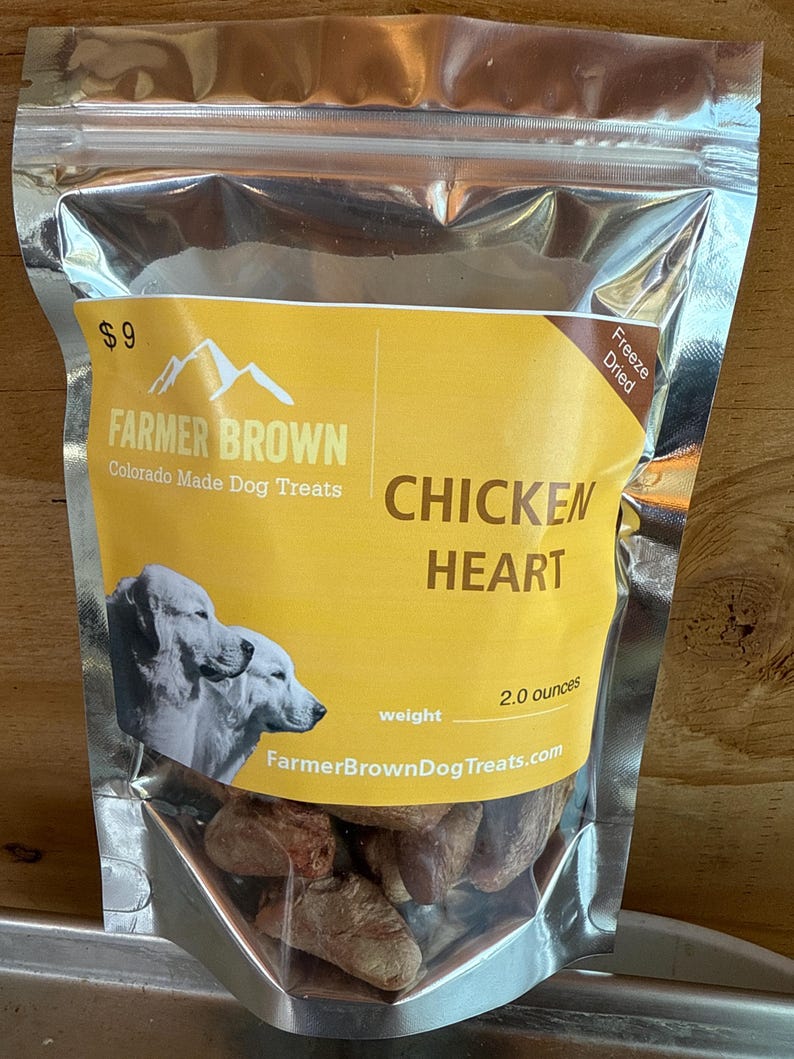 May include: A silver metallic bag of Farmer Brown Chicken Heart dog treats. The bag has a yellow label with the text "CHICKEN HEART" and a weight of 57 grams. The bag also features a picture of two dogs.