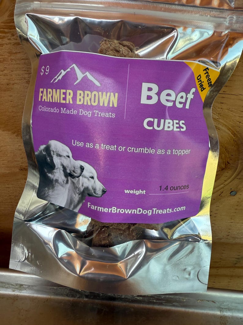 May include: A sealed silver bag of Farmer Brown Beef Cubes dog treats. The purple label features the brand name, a mountain graphic, and the text "Colorado Made Dog Treats." The bag contains 1.4 ounces of freeze-dried beef cubes.