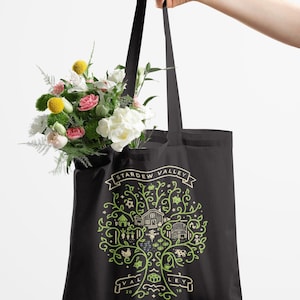May include: Black tote bag featuring a green and white graphic of a tree with farm elements and the text "Stardew Valley". The bag is filled with a bouquet of flowers. The bag is held by a person.