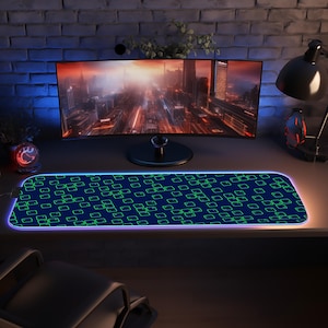 May include: A rectangular, blue and green patterned gaming mouse pad with a glowing edge. The pad features a repeating pattern of green squares and rectangles. A computer monitor and desk lamp are in the background.