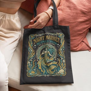 Black tote bag with "Night Market Mermaid Show" text and stylized mermaid artwork.