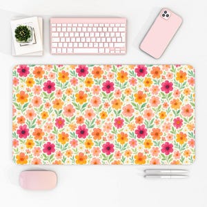 Peut inclure: Tapis de bureau à motifs floraux avec un motif répété de fleurs orange, roses et jaunes avec des feuilles vertes sur fond blanc. Un clavier, une souris et un téléphone roses sont également visibles.