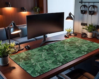 May include: A large, rectangular desk mat with a green leaf pattern. The mat is placed on a dark wooden desk, with a computer monitor, desk lamp, and potted plants. The mat's design features a repeating pattern of stylized leaves.