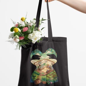 May include: Black tote bag featuring a colourful illustration of a clinic and garden scene. The bag is held by a hand and filled with a bouquet of flowers. The illustration includes the text "Harvey's Clinic".