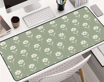 Puede incluir: Alfombrilla de escritorio rectangular con un diseño floral. La alfombrilla tiene un fondo verde claro con un patrón repetido de flores blancas. Tiene un borde negro y está colocada sobre un escritorio blanco.
