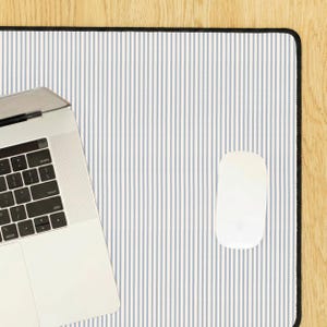 May include: A white computer mouse and a laptop rest on a mouse mat with blue and white vertical stripes and a black border. The mat is on a wooden surface.