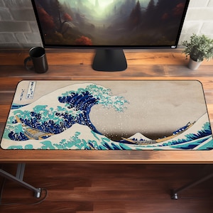 Puede incluir: Una alfombrilla de ratón rectangular con la icónica obra de arte japonesa "La gran ola de Kanagawa". El diseño muestra una gran ola estilizada en tonos azules y blancos, con barcos y el monte Fuji al fondo. La alfombrilla está sobre un escritorio de madera.