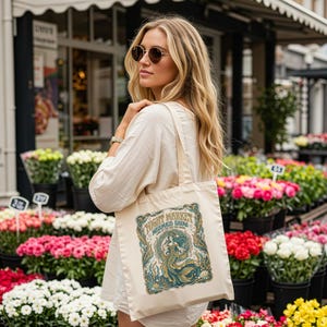 Woman holding tote bag with "Night Market Mermaid Show" graphic near flower stands.