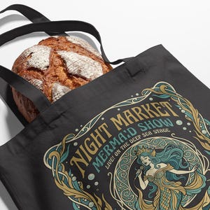 Black tote bag with a colorful "Night Market Mermaid Show" graphic.