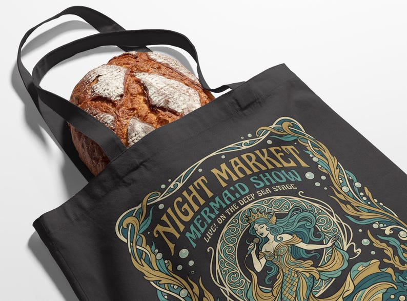 Black tote bag with a colorful "Night Market Mermaid Show" graphic.