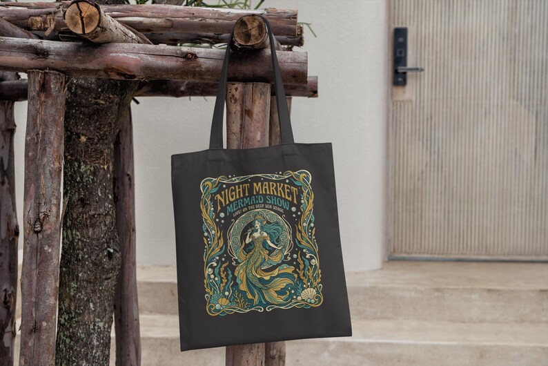 Black tote bag with a vintage mermaid illustration and "Night Market Mermaid Show" text.