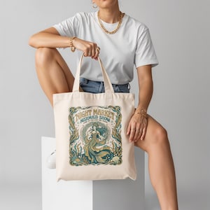 Cream canvas tote bag with a mermaid show design and text.
