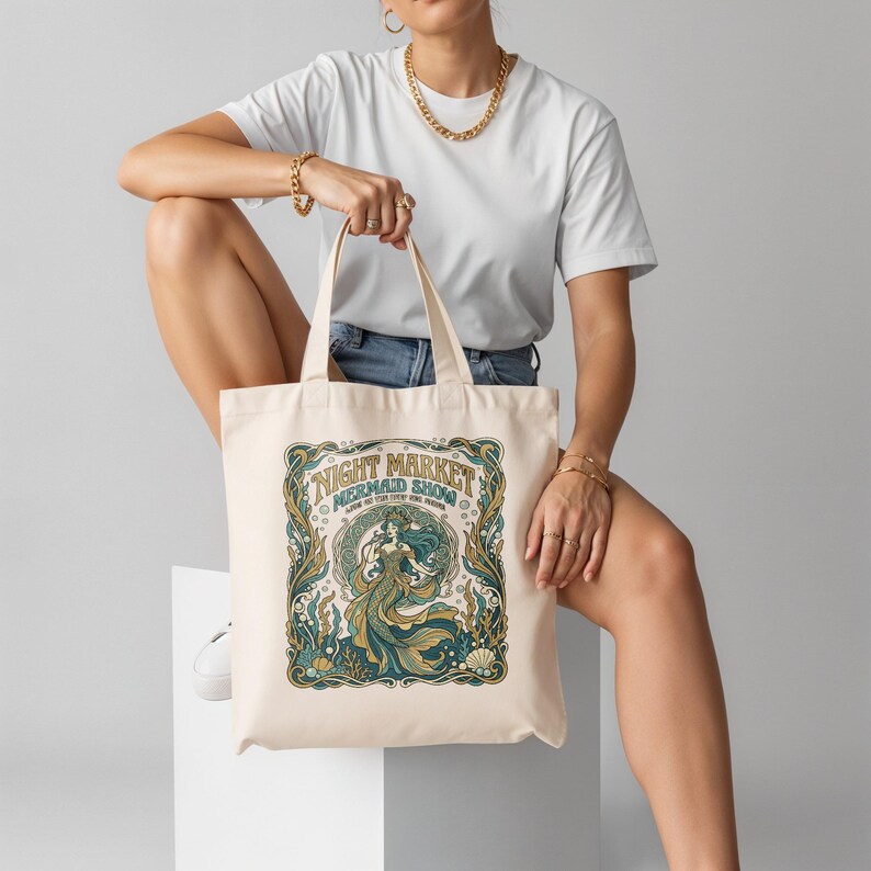 Cream canvas tote bag with a mermaid show design and text.