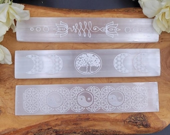 May include: Three rectangular selenite crystal wands with etched designs. The top wand features a lotus and flowing lines, the middle one has a tree of life and crescent moons, and the bottom one displays a yin-yang symbol.