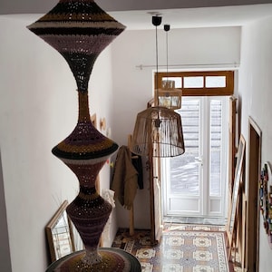 Peut inclure: Une lampe suspendue en crochet multicolore avec un design unique est suspendue au plafond dans un couloir avec un sol en carrelage à motifs. Deux lampes suspendues en osier pendent du plafond au-dessus d'une porte.