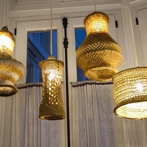 May include: Four crocheted lampshades hanging from the ceiling. The lampshades are made of a light brown yarn and have a variety of shapes, including a cylinder, a vase, and a bell.