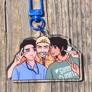 May include: A clear acrylic keychain featuring a cartoon illustration of three people. The keychain has a blue clasp. One person wears a blue shirt, another an orange jacket, and the third a green shirt with the text "Sunny Climate".
