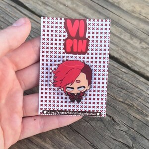 Pode incluir: Pin com um personagem de desenho animado com cabelo vermelho e express&atilde;o determinada. O pin est&aacute; em um cart&atilde;o com um padr&atilde;o repetido de cruzes marrons e o texto "VI PIN". O URL da loja Etsy &eacute; vis&iacute;vel.