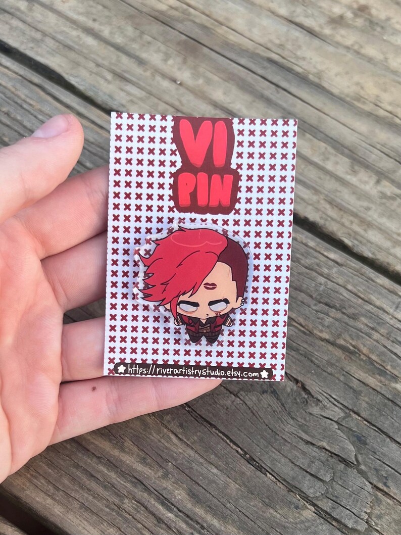 Pode incluir: Pin com um personagem de desenho animado com cabelo vermelho e express&atilde;o determinada. O pin est&aacute; em um cart&atilde;o com um padr&atilde;o repetido de cruzes marrons e o texto "VI PIN". O URL da loja Etsy &eacute; vis&iacute;vel.
