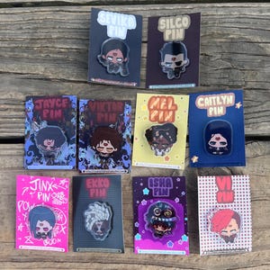 May include: A selection of character pins, each presented on a card. The pins depict stylized illustrations of characters with names including "Sevika," "Silco," "Jayce," "Viktor," "Mel," "Caitlyn," "Jinx," "Ekko," "Isha," and "Vi." The pins are vibrant and detailed.