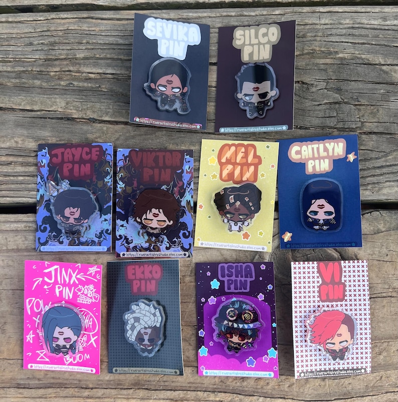 Pode incluir: Uma cole&ccedil;&atilde;o de pins de personagens, cada um montado em um cart&atilde;o. Os pins apresentam ilustra&ccedil;&otilde;es estilizadas de personagens com nomes como "Sevika", "Silco", "Jayce", "Viktor", "Mel", "Caitlyn", "Jinx", "Ekko", "Isha" e "Vi". Os pins s&atilde;o coloridos e detalhados.