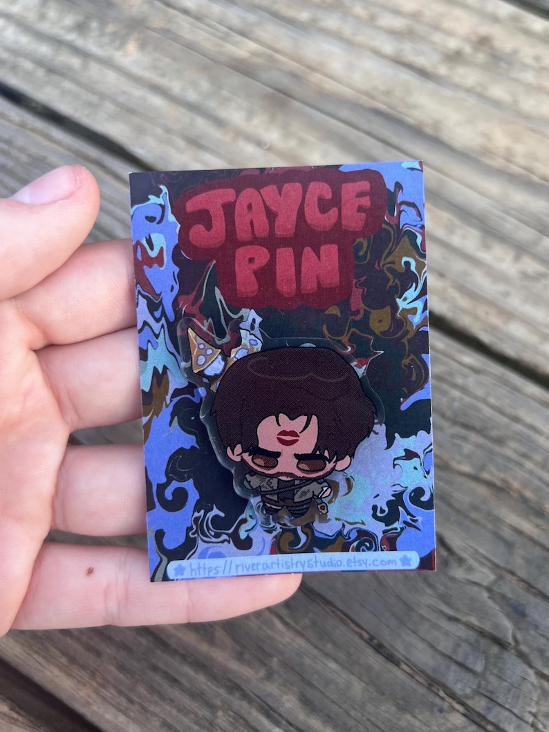 Pode incluir: Um alfinete com um personagem de desenho animado com cabelo castanho e um design de l&aacute;bios vermelhos. O alfinete est&aacute; em um cart&atilde;o com as palavras "JAYCE PIN" em letras vermelhas. O cart&atilde;o tem um design abstrato azul e marrom e o URL da loja Etsy.