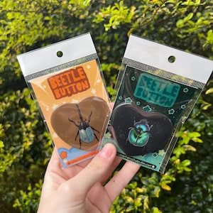 May include: Two heart-shaped beetle buttons in clear plastic packaging. One button is brown with a beetle illustration and the text "BEETLE BUTTON" in orange. The other is black with a beetle illustration and the text "BEETLE BUTTON" in teal.