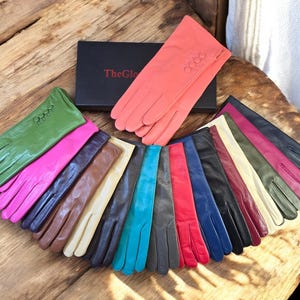 Könnte beinhalten: Eine Sammlung von 14 Paar Lederhandschuhen in verschiedenen Farben, darunter Grün, Pink, Braun, Beige, Blau, Türkis, Rot und Schwarz. Die Handschuhe haben ein Knopfdetail am Handgelenk.