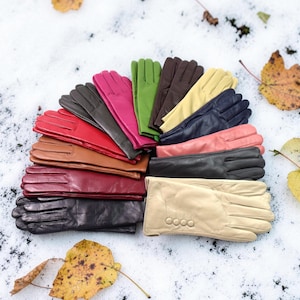 May include: A collection of leather gloves arranged in a fan shape, featuring a variety of colors including black, red, brown, pink, green, dark brown, yellow, navy blue, coral, and beige, with the beige pair displaying four decorative buttons.